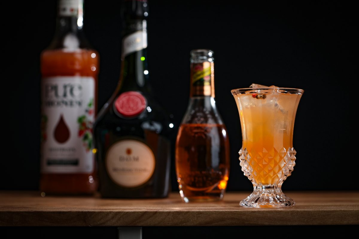 Cocktail orange sur noir, avec une bouteille de schwepps en arrière plan